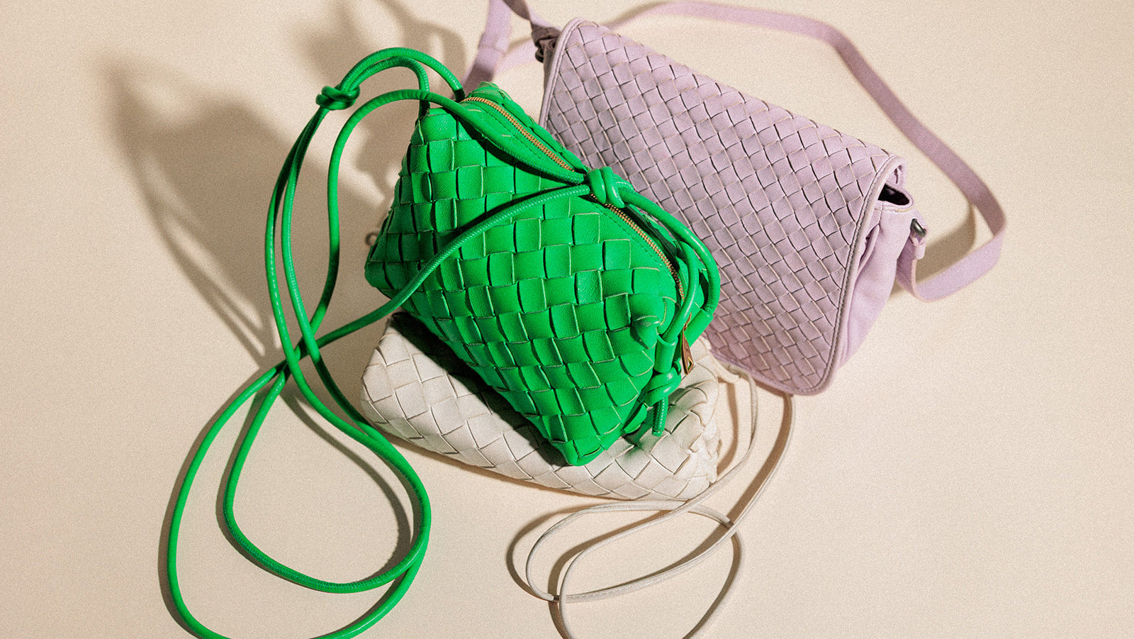 Three woven handbags in green, white, and purple on a beige background