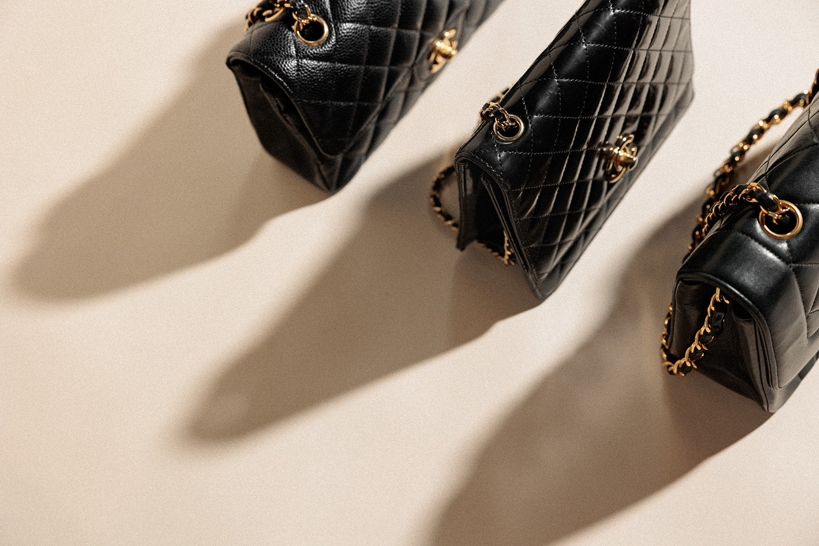 Black quilted handbags with gold chains on a beige background